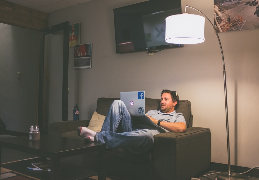 man lying on couch while using laptop computer