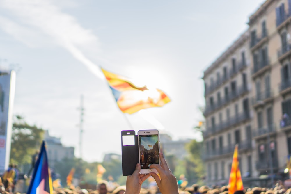 person taking photo of yellow and blue flag through silver iPhone 6 with black flip case during daytime