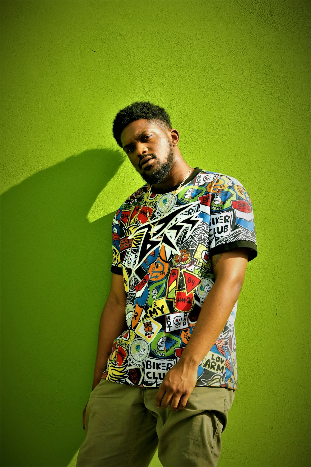 man wearing multicolored artwork crew-neck t-shirt leaning on green painted concrete wall