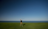 A boy taking a confident swing with a golf club in a green field.