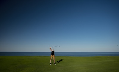 A boy practicing his golf swing on a green field, wearing a big grin with his new clubs.