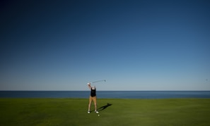 A boy taking a confident swing with a golf club in a green field.