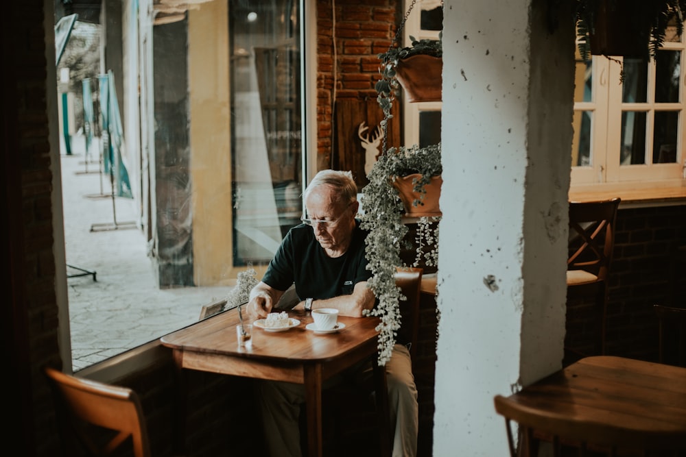 Un homme en chemise noire est assis à l’intérieur d’un restaurant avec du café sur le devant