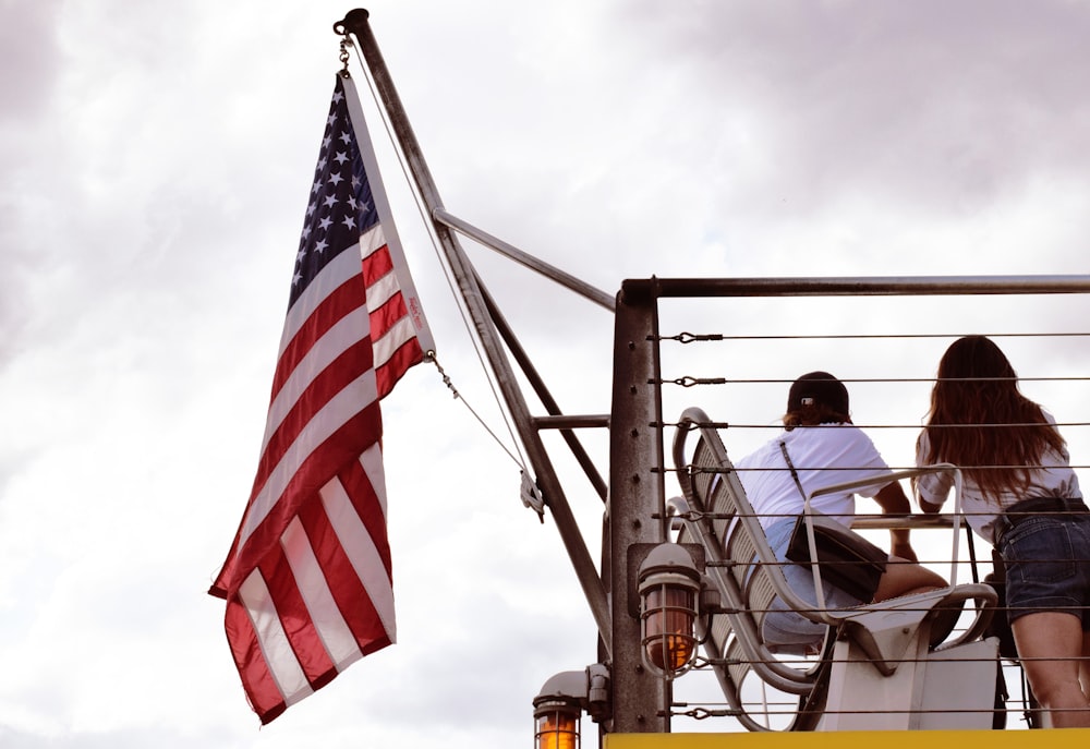Hombre con chaqueta negra sentado en una silla cerca de la bandera de EE. UU. durante el día