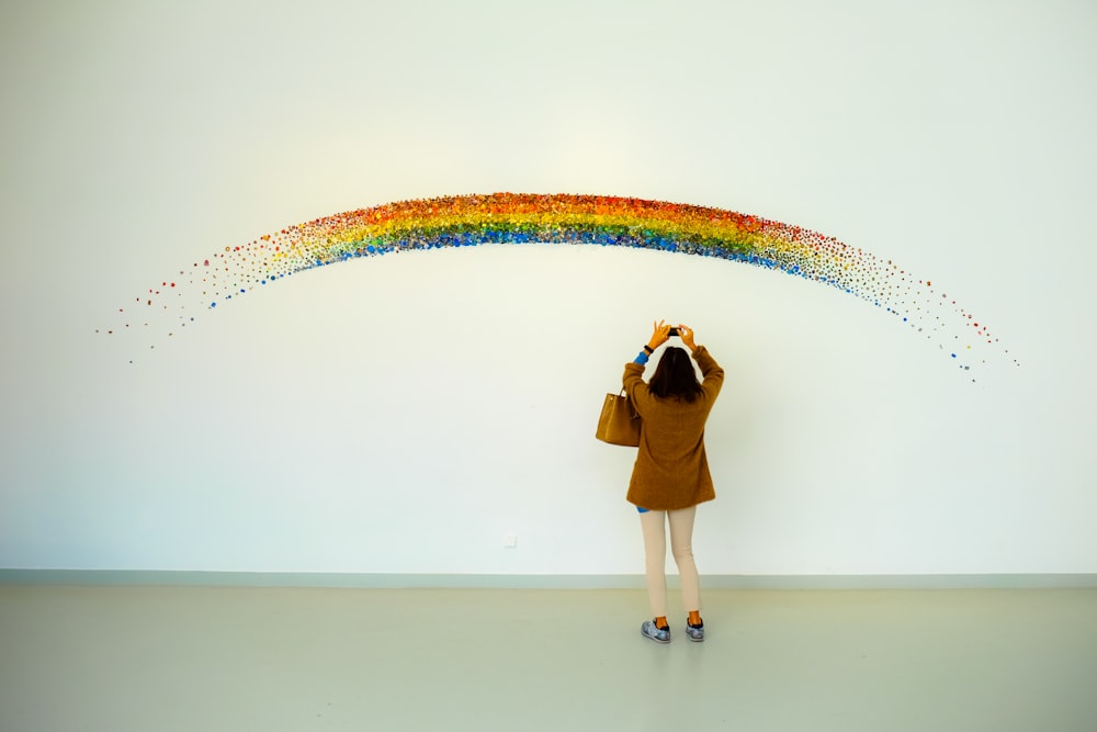woman wearing brown jacket standing front of rainbow painting taking photo