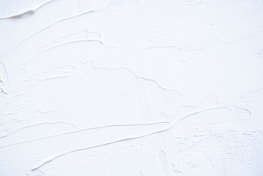 White textured surface with smooth and rough patches, possibly resembling thick paint or plaster applied onto a flat surface. The surface has visible brush or tool marks, creating a sense of movement and dimension.