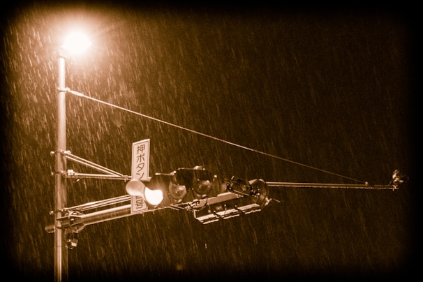 A moody shot of a Japanese street sign flickering in the rain with neon reflections.