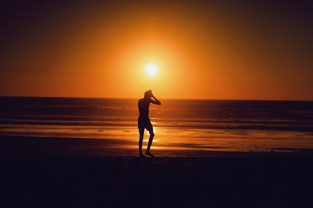 silhouette of person beside seashore during sunset