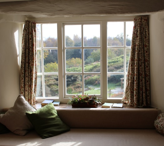 large window with curtains open wide, looking out onto a lush country side scene
