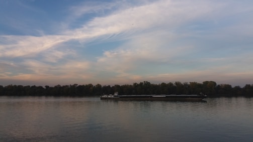 A blue and white inland cargo ship named Libertas sailing on a calm river under a cloudy sky.