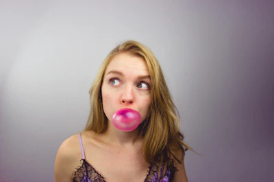 A badass woman wearing bubblegum pink faux fur and blowing a big bubblegum bubble, holding a pink felt pennant with a feminist slogan.