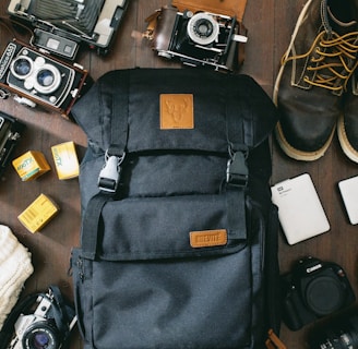 high-angle photo of black bag beside cameras, portable HDD and black leather lace-up boots