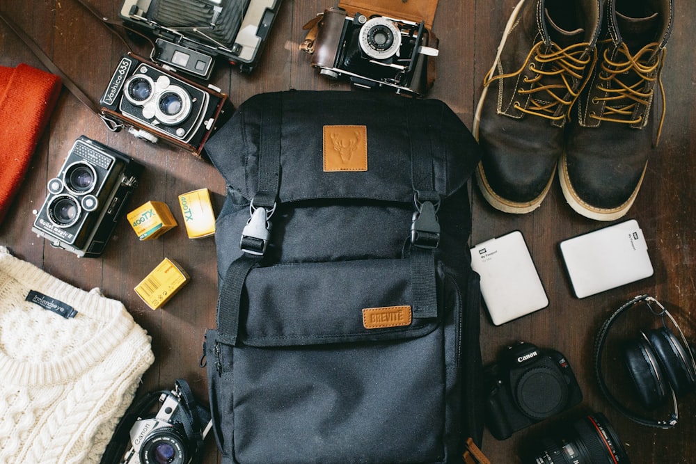 photo en plongée d’un sac noir à côté d’appareils photo, d’un disque dur portable et de bottes à lacets en cuir noir