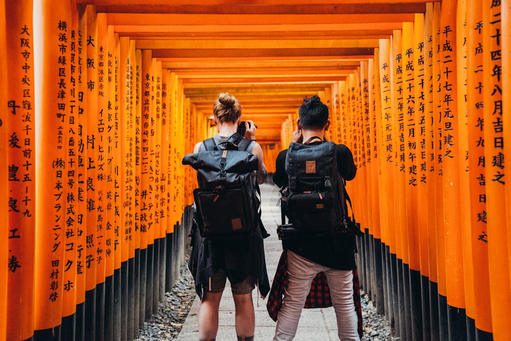 オレンジ色の漢字テキストプリントの壁の下に立つ男性と女性