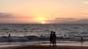 A honeymoon couple sharing a romantic sunset on a beach with warm orange hues.