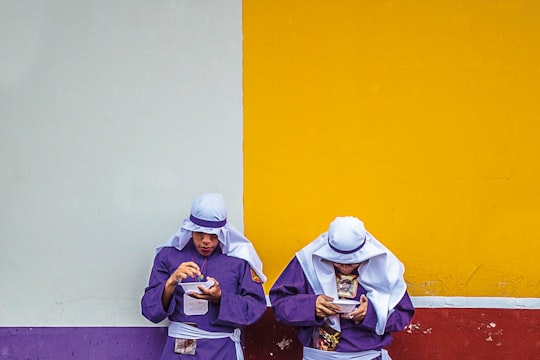 two standing men wearing purple long-sleeved top leaning on white, yellow, purple, and red painted wall in Antigua Guatemala Guatemala