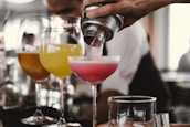 person holding cocktail shaker pouring liquid in glass during daytime