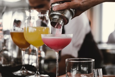 person holding cocktail shaker pouring liquid in glass during daytime