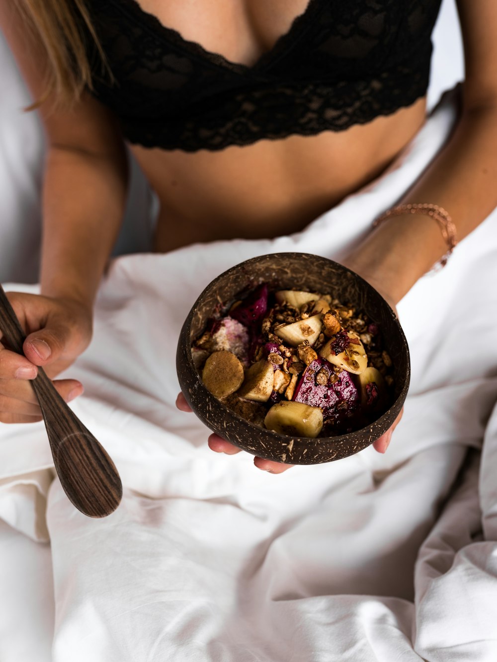 geschnittene Früchte auf Kokosnussschalenschale auf Frauenhand im Bett
