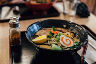 focus photography of ramen in bowl with condiment shakers