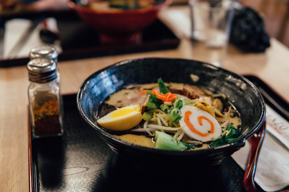 focus photography of ramen in bowl with condiment shakers