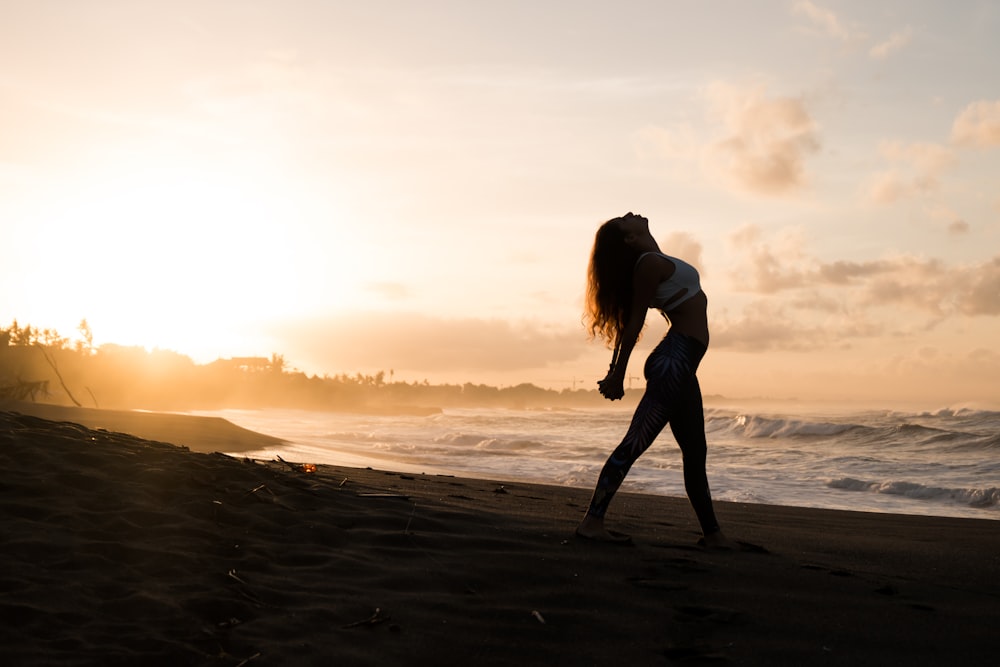 Silhouette einer Frau, die während des Sonnenaufgangs ihre Arme am Meeresufer ausstreckt