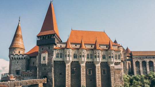 gray and orange concrete structure under blue sky during day in Hunyad Castle Romania