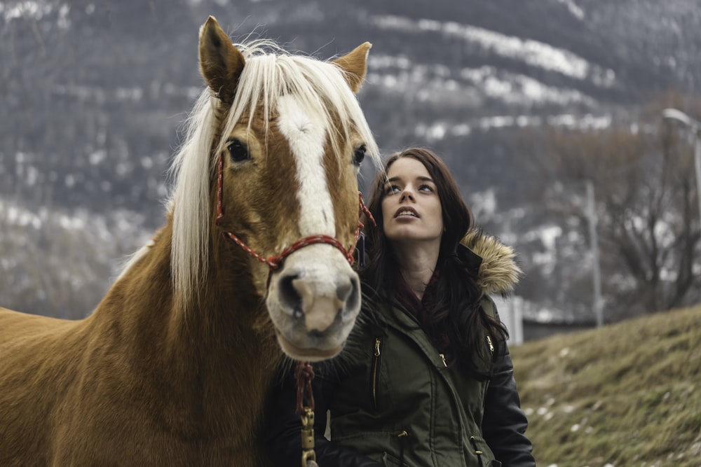 woman in green parka jacket standing beside brown horse