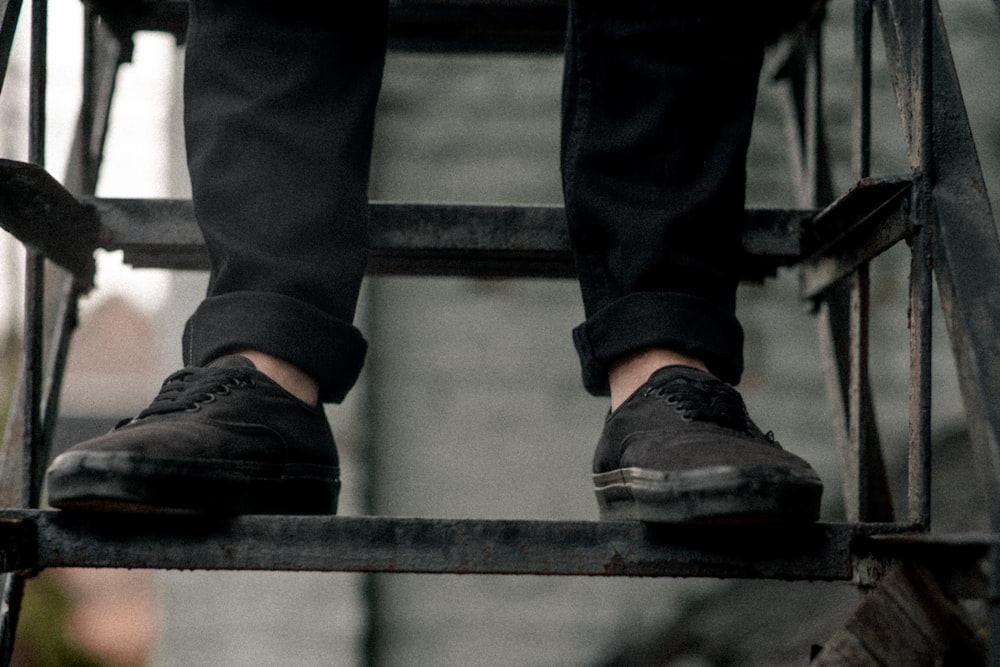 person wearing pair of black low-top sneakers on staircase