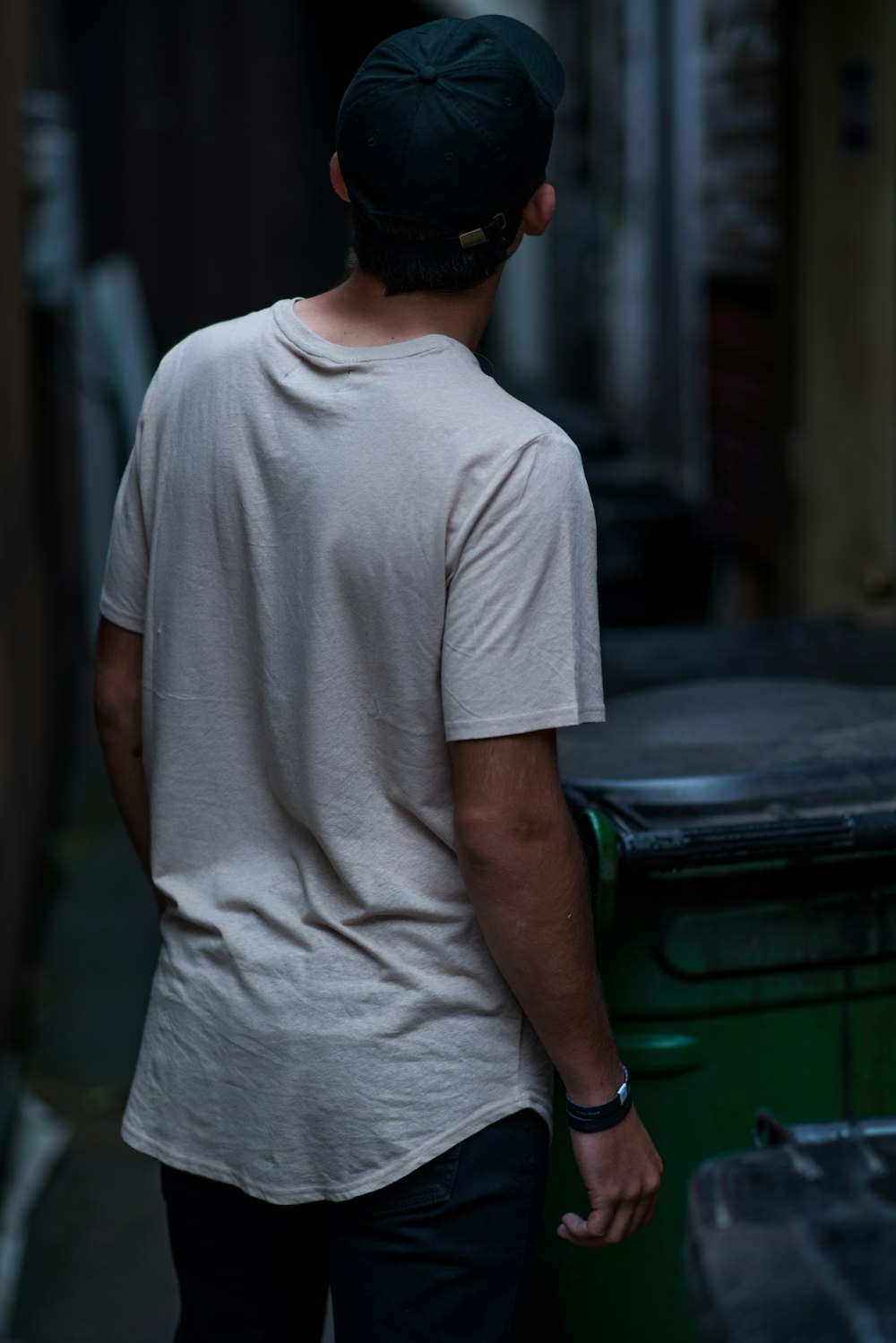 man wearing white shirt beside wheelie bin