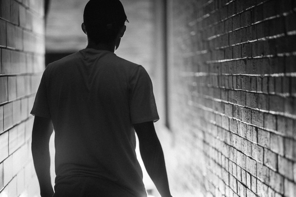 grayscale photo of man between shingle wall