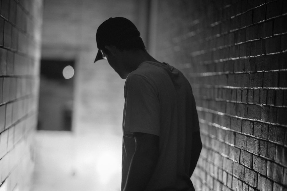 photography of man looking down surrounded by brick walls