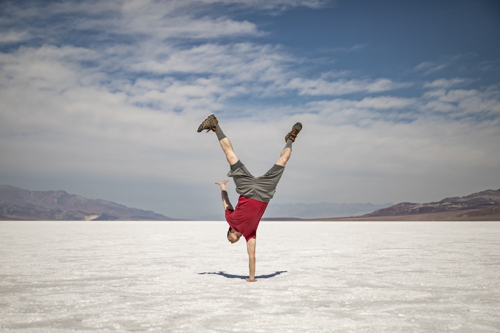 man doing one hand stand under white skies at daytime