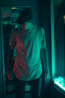 Model wearing a black cap and oversized tee under neon city lights