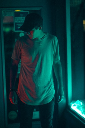 Model wearing a neon orange cap and off-white t-shirt standing in a dimly lit alley with futuristic lighting.