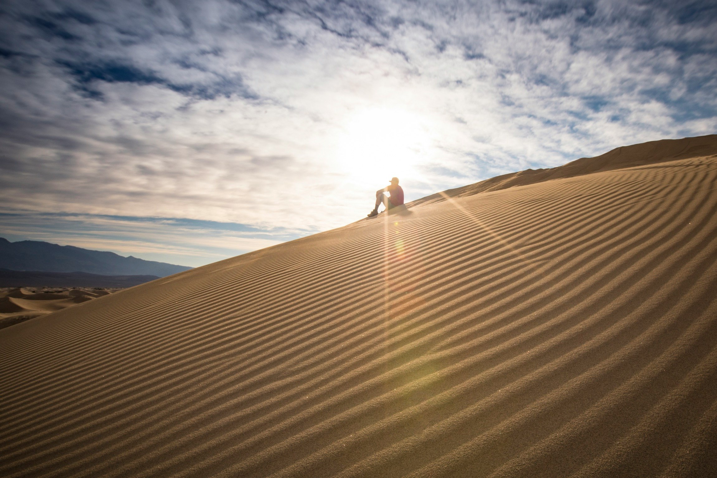 person in black jacket walking on desert under blue and white sunny cloudy sky during daytime