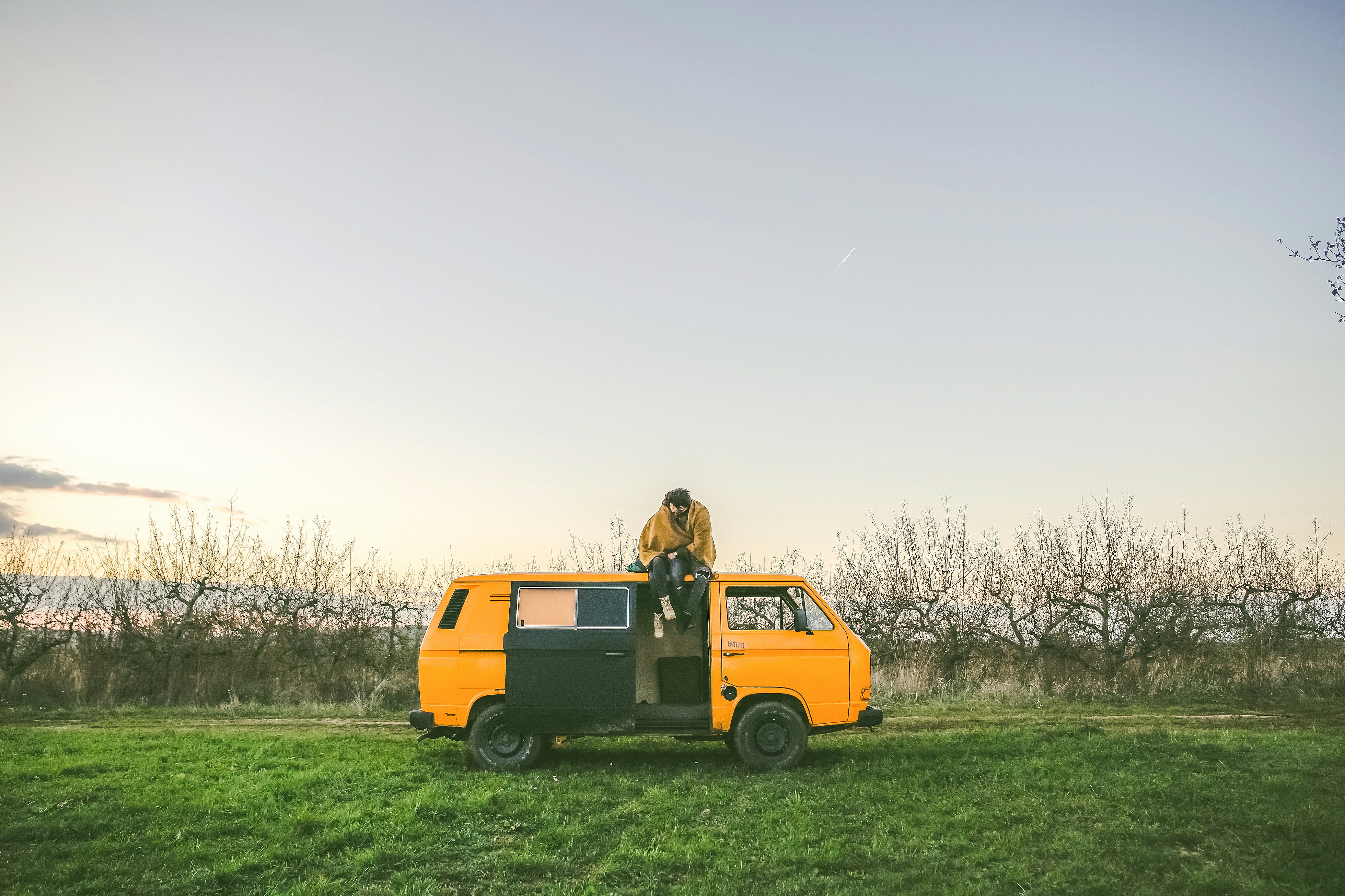 person sitting on top of yellow van on grass field during day