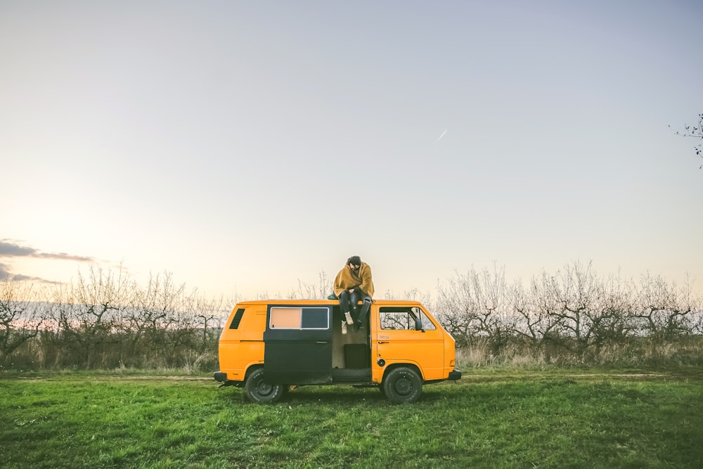 person sitting on top of yellow van on grass field during day
