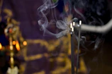 Close-up of glowing incense sticks releasing gentle smoke against a warm saffron background.