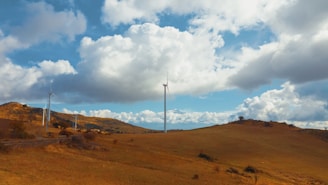 Tall white wind turbines turning gracefully against a backdrop of rolling green hills.