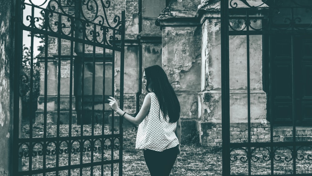 grayscale photo of standing woman beside metal gate