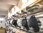 A retail display features a variety of caps organized on glass shelves, with colors including black, white, and pink. Additional accessories such as sunglasses and keychains are arranged below. The store has modern lighting and a dreamcatcher hanging on one side.