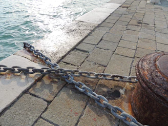 Rust-resistant marine bollard gleaming in the sunlight beside a calm harbor with boats tied securely.