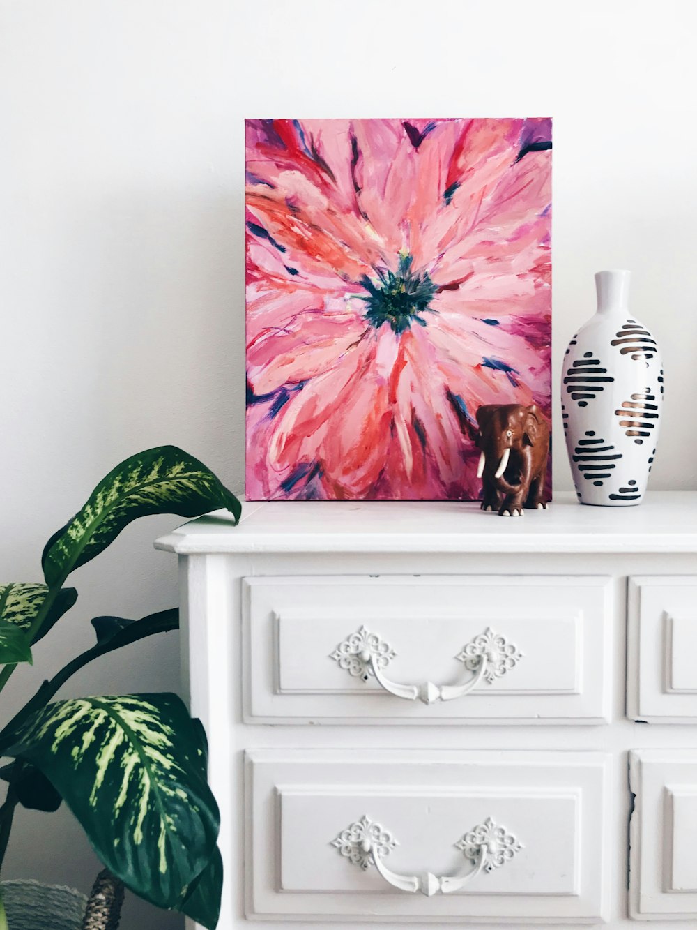Gemälde einer rosa Blume auf einer Kommode in der Nähe einer weißen Vase