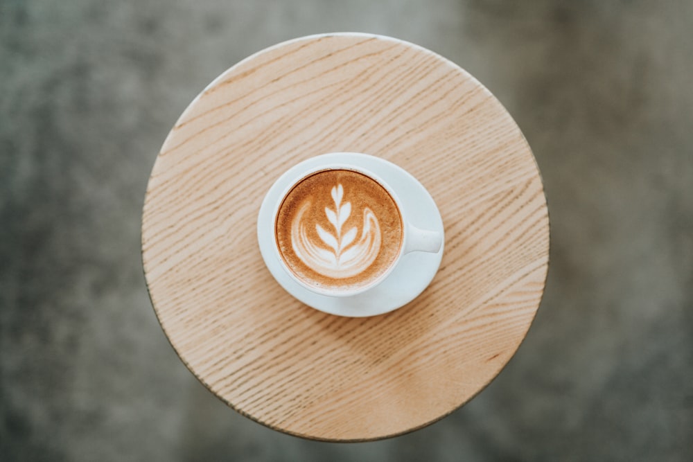 cappuccino on white ceramic mug with saucer on round brown coaster