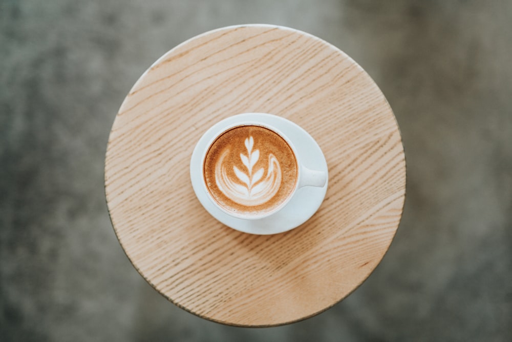 Cappuccino em caneca de cerâmica branca com pires em montanha-russa marrom redonda