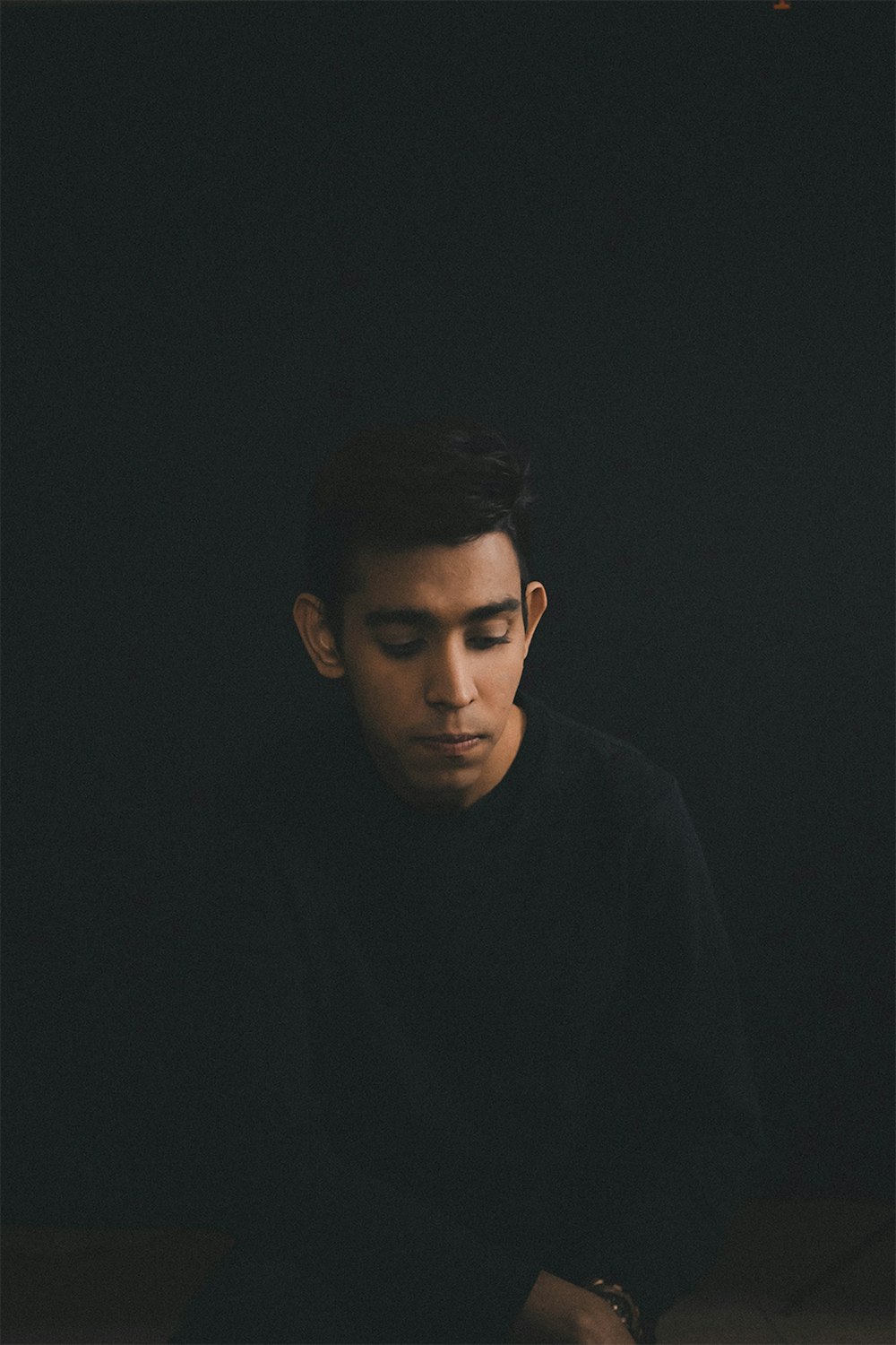 man wearing black long-sleeved shirt sitting while looking down