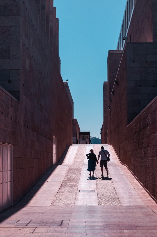 two man and woman walking on pathway between buildings in Centro Cultural de Belém Portugal