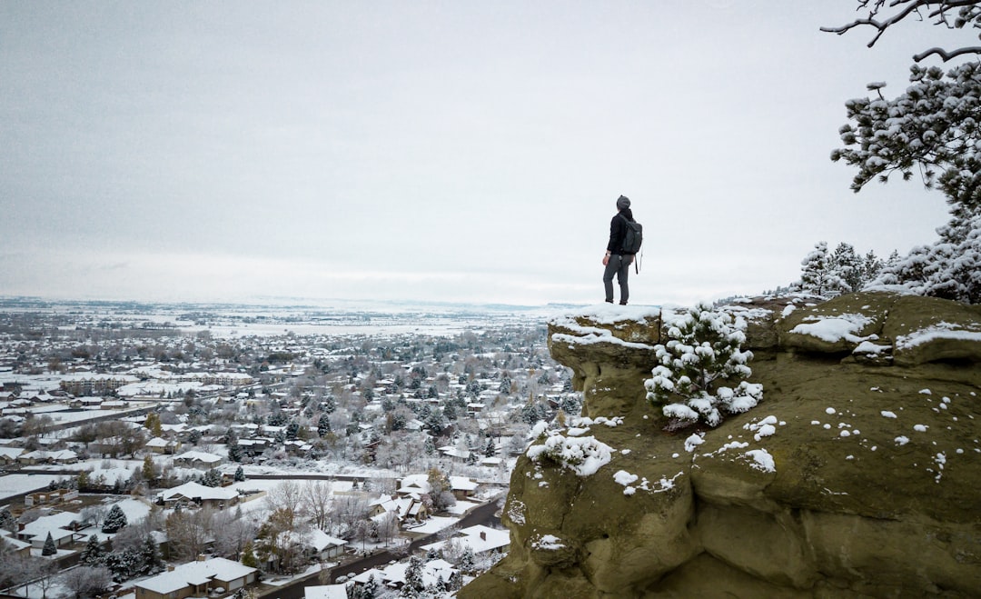 person standing on cliff of gray rocky mountain with snow during daytime