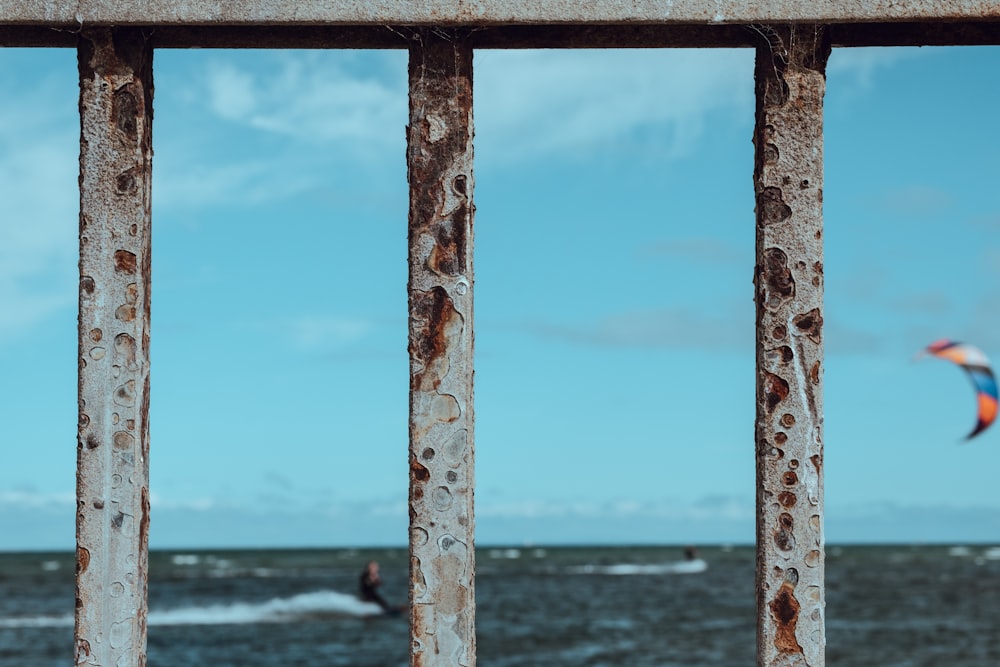 focus photography of rusted fence near beach with surf wind gliding background